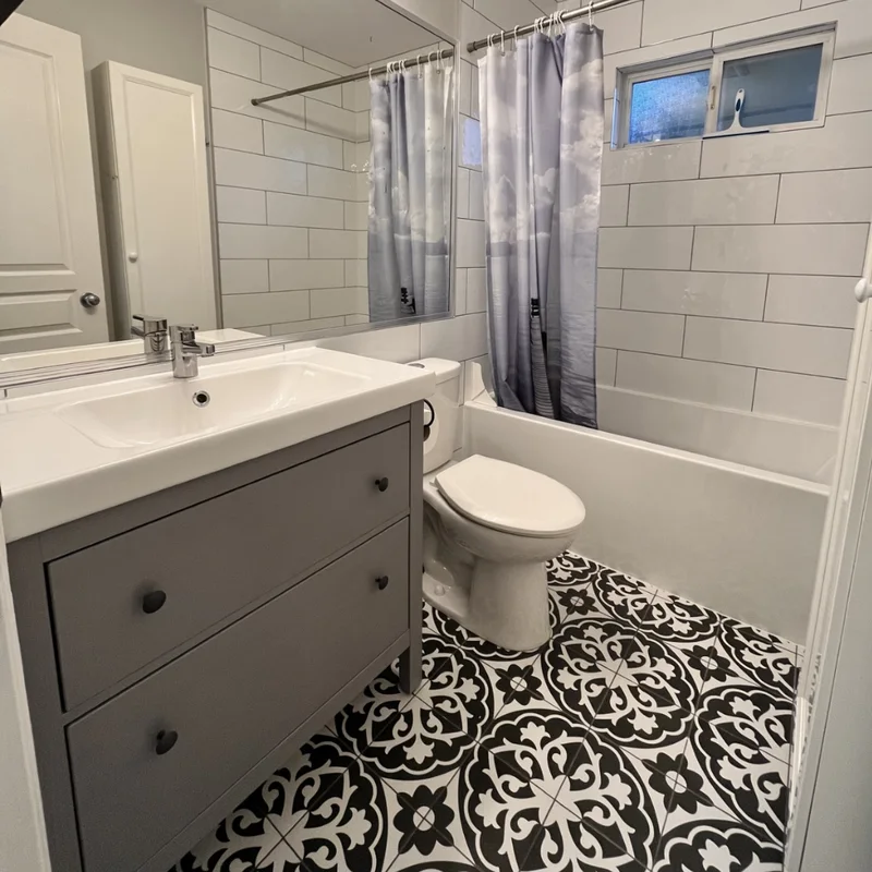 A finished bathroom renovation with a grey vanity and black-and-white patterned floor tiles