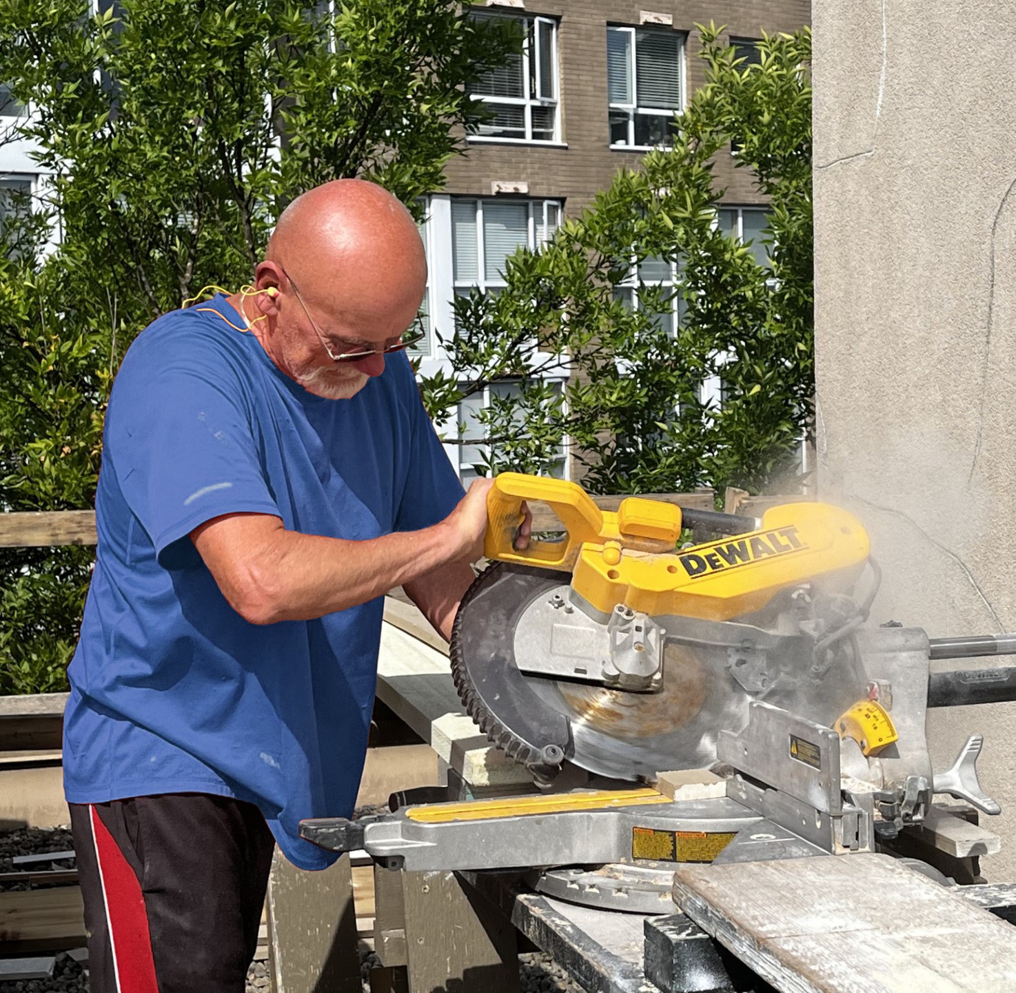 Recap crew member in ear protection cutting lumber on a mitre saw at a jobsite